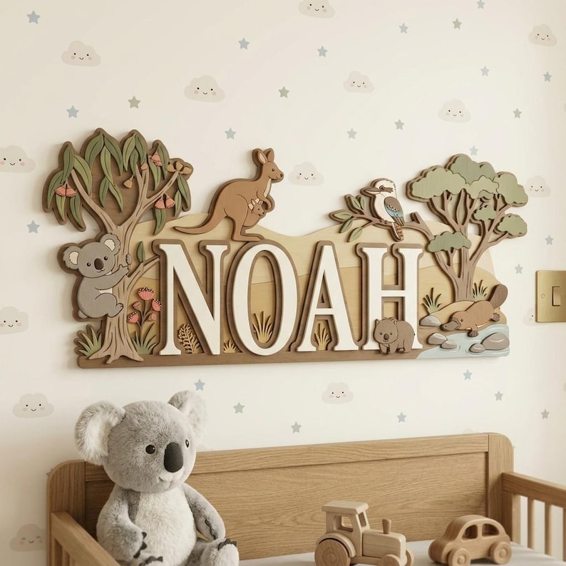May include: A wooden wall decoration spelling "NOAH" with an Australian theme. The design includes a koala, kangaroo, kookaburra, wombat, and platypus, along with trees and foliage. The letters are white with a brown border.