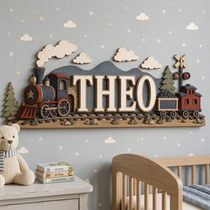 Könnte beinhalten: Eine Wanddekoration aus Holz mit einer Lokomotive, einem Güterwagen und dem Namen THEO in großen weißen Buchstaben. Die Szene zeigt ein dunkelblaues Gebirge, grüne Tannen, ein Bahnübergangssignal und helle Wolken am oberen Rand.