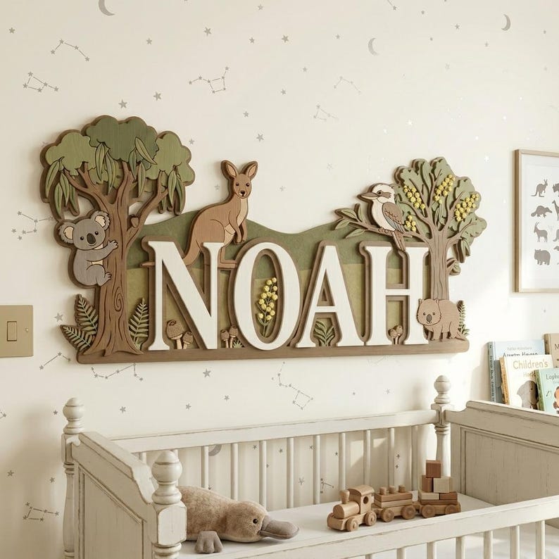 May include: A wooden wall sign spelling "NOAH" in white letters, with a koala, kangaroo, and kookaburra. The sign has a green and brown color scheme, with trees and other Australian flora and fauna. The sign is above a white crib.