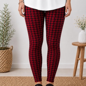 May include: Full-length leggings featuring a classic red and black houndstooth pattern. The leggings are form-fitting and extend from the waist down to the ankles, paired with black slide sandals that have a braided strap design across the top.