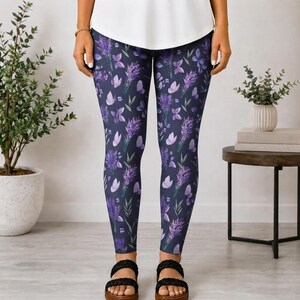 May include: Full-length leggings in a dark navy blue base color featuring a repeating pattern of purple lavender sprigs and small light purple butterfly shapes. The leggings have a fitted silhouette and are paired with a plain white top.