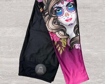 May include: Black leggings with a sugar skull design. The leggings feature a colorful graphic of a woman's face with floral accents and a gradient from purple to pink. The brand logo is visible on the black portion of the leggings.