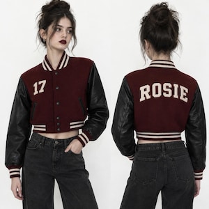 May include: A cropped varsity jacket featuring a maroon wool-blend body and black sleeves. The front displays the number 17 in white, while the back features the name ROSIE in white lettering. It includes a striped ribbed collar, cuffs, and hem.