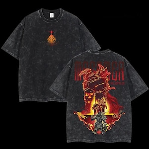 May include: Black acid wash t-shirt featuring a graphic design on the front and back. The front has a gold and red emblem. The back displays a red and gold illustration with the text "MAGNUM THE IMPALER".