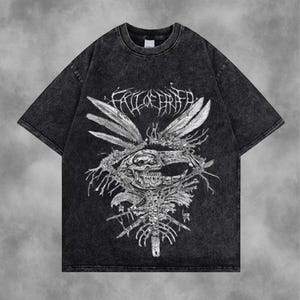 Puede incluir: Camiseta gris oscuro con acabado desgastado. El frente presenta un gráfico blanco detallado de una calavera, plumas y elementos esqueléticos. El texto "FALL OF FAITH" está arqueado sobre el diseño central.