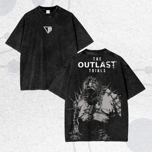 Könnte beinhalten: Zwei schwarze T-Shirts mit einem verwaschenen, Vintage-Look. Eines zeigt ein weißes geometrisches Logo, das andere den Text "THE OUTLAST TRIALS" über einer detaillierten Grafik einer Figur mit Stacheln.