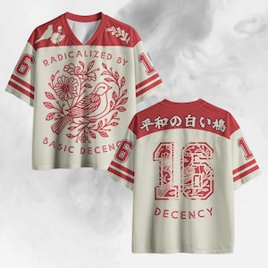 Könnte beinhalten: Cremefarbenes Trikot mit roten Akzenten und V-Ausschnitt. Auf der Vorderseite befindet sich ein Vogel- und Blumendesign mit dem Text "RADICALIZED BY BASIC DECENCY". Auf der Rückseite ist die Zahl "16" mit floralen Details und dem Wort "DECENCY" zu sehen.