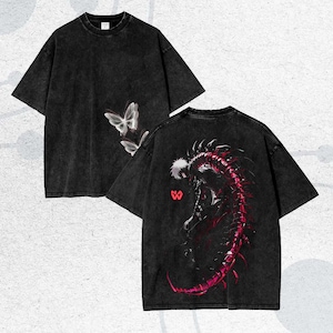 Puede incluir: Dos camisetas negras con efecto lavado descolorido. Una camiseta presenta un gráfico de mariposa, la otra un diseño de criatura roja y negra. Ambas camisetas tienen mangas cortas y cuello redondo.