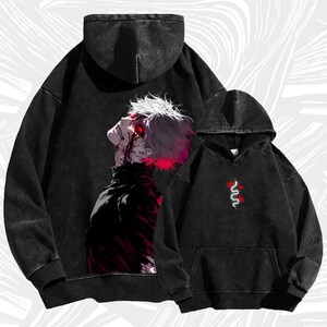 Puede incluir: Dos sudaderas con capucha negras. Una presenta un gráfico de un personaje con cabello blanco y detalles rojos. La otra tiene un diseño de serpiente roja y blanca. Ambas tienen un aspecto vintage desgastado.