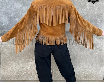 Puede incluir: Chaqueta de ante marrón con flecos en la espalda y las mangas. La chaqueta tiene cuello y una silueta entallada. Los flecos añaden un toque bohemio al diseño clásico. La chaqueta se lleva con vaqueros negros y botas marrones.