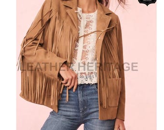 Puede incluir: Chaqueta de ante marrón claro con flecos en las mangas y el pecho. La chaqueta tiene un corte de blazer clásico con bolsillos y se combina con una blusa de encaje blanca y vaqueros azules. El logo "Leather Heritage" es visible.