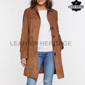 May include: A brown suede trench coat with a button-up front, long sleeves, and a collar. The coat is worn over a white top and blue jeans. The image includes the text "LEATHER HERITAGE".
