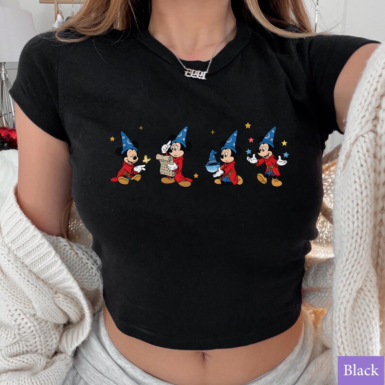 Puede incluir: Top corto negro con un gr&aacute;fico colorido de Mickey Mouse con un disfraz de mago. El dise&ntilde;o muestra a Mickey en diferentes poses con un sombrero de mago azul, una t&uacute;nica roja y estrellas. La camiseta es de manga corta.