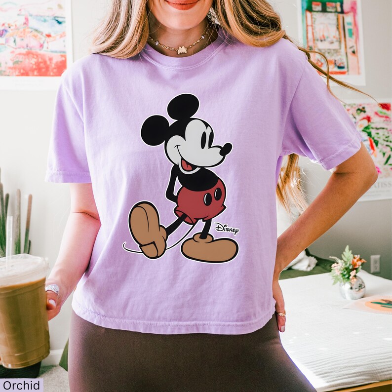 K&ouml;nnte beinhalten: Ein helllila T-Shirt mit einer Mickey Mouse-Grafik. Die Cartoonfigur ist in Schwarz, Wei&szlig;, Rot und Braun gehalten, mit dem Disney-Logo. Das T-Shirt ist ein l&auml;ssiger Stil, geeignet f&uuml;r den Alltag.