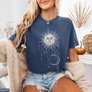 Puede incluir: Una camiseta de manga corta azul oscuro con un estampado gr&aacute;fico blanco de un sol con cara, una luna creciente y estrellas colgantes conectadas por l&iacute;neas finas. La camiseta tiene cuello redondo y se lleva con pantalones cortos de mezclilla.