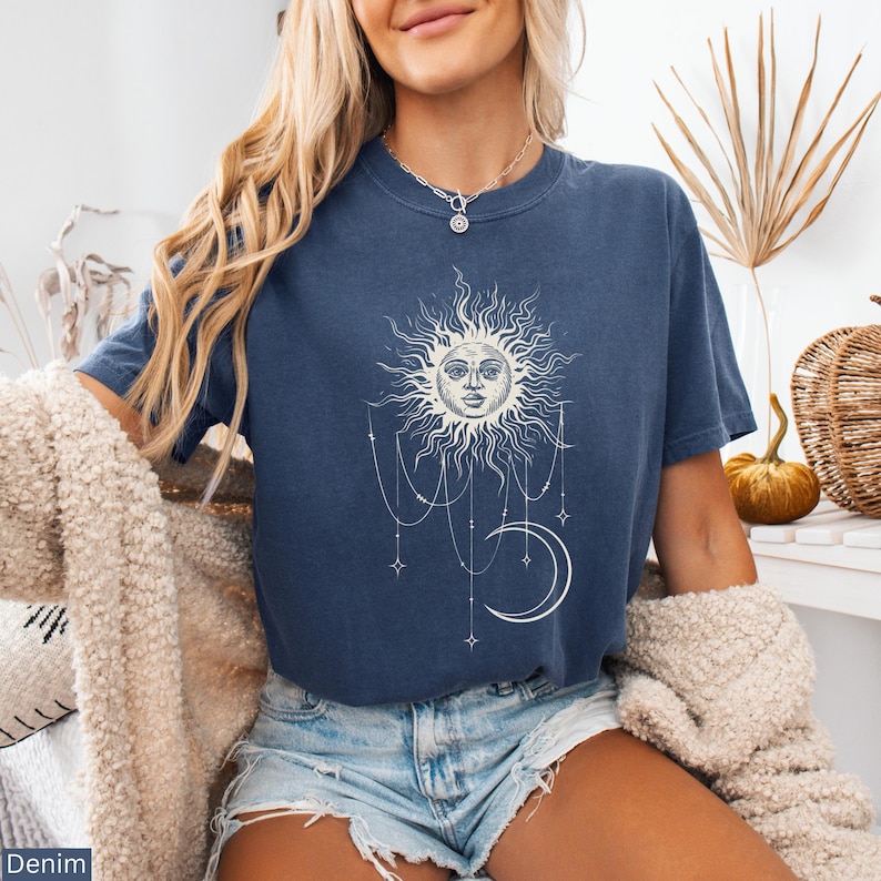 Puede incluir: Una camiseta de manga corta azul oscuro con un estampado gr&aacute;fico blanco de un sol con cara, una luna creciente y estrellas colgantes conectadas por l&iacute;neas finas. La camiseta tiene cuello redondo y se lleva con pantalones cortos de mezclilla.