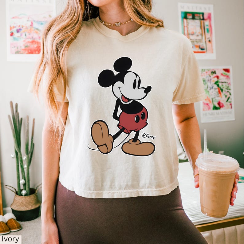 K&ouml;nnte beinhalten: Elfenbeinfarbenes T-Shirt mit Mickey Mouse-Grafik. Die Cartoonfigur ist in Schwarz, Wei&szlig;, Rot und Braun gehalten, mit dem Disney-Logo. Das T-Shirt hat eine lockere Passform. Das Wort "Ivory" ist unten links aufgedruckt.