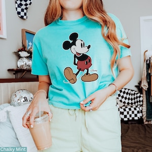 K&ouml;nnte beinhalten: Ein t&uuml;rkisfarbenes T-Shirt mit einer Mickey Mouse-Grafik. Die Zeichentrickfigur ist in Schwarz, Rot und Beige gehalten, mit dem Disney-Logo. Das Shirt ist mit "Chalky Mint" beschriftet.