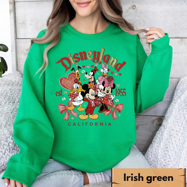 May include: Green sweatshirt with a Disneyland graphic featuring Mickey Mouse, Minnie Mouse, Donald Duck, Daisy Duck, Goofy, and Pluto. The graphic includes the text "Disneyland est. 1955 California" in red and white.