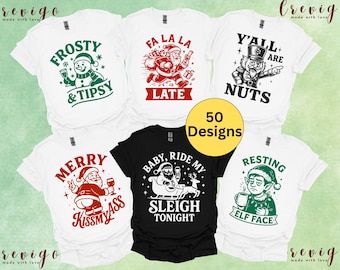 May include: A collection of white and black t-shirts with various Christmas-themed graphics. Designs include a snowman with a drink, Santa Claus, and an elf. The text on the shirts includes phrases like "Frosty & Tipsy" and "Y'all are Nuts."