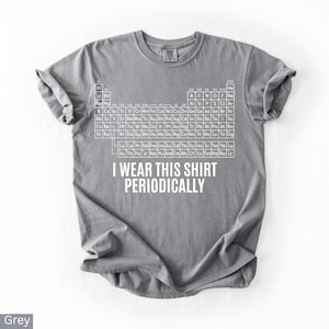 May include: A grey t-shirt with a white periodic table of elements design. The shirt has the text "I WEAR THIS SHIRT PERIODICALLY" printed below the table. The shirt is made of a soft material.