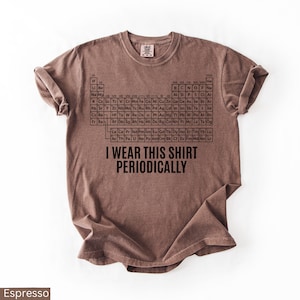 May include: Espresso-colored t-shirt featuring a black periodic table design and the phrase "I WEAR THIS SHIRT PERIODICALLY." The shirt is a short-sleeved, crew neck style, perfect for science enthusiasts.