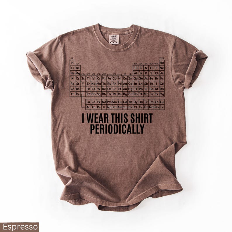 May include: Espresso-colored t-shirt featuring a black periodic table design and the phrase "I WEAR THIS SHIRT PERIODICALLY." The shirt is a short-sleeved, crew neck style, perfect for science enthusiasts.