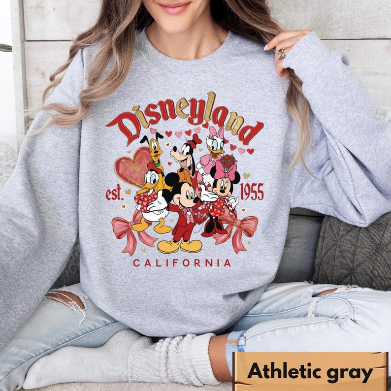 May include: Grey sweatshirt with a Disneyland graphic featuring Mickey and Minnie Mouse, Donald Duck, Goofy, Pluto, and Daisy Duck. The design includes the text "Disneyland California est. 1955" in red and white.
