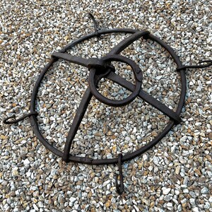 May include: A vintage metal cage with a circular base and four hooks. The cage is made of black metal and has a ring in the center.