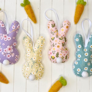 Pu&ograve; includere: Quattro decorazioni di coniglio in feltro fatte a mano con diversi motivi floreali. I conigli sono viola, giallo, rosa e blu. Ogni coniglio ha una coda di pon pon bianca.