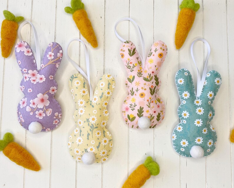 Pu&ograve; includere: Quattro decorazioni di coniglio in feltro fatte a mano con diversi motivi floreali. I conigli sono viola, giallo, rosa e blu. Ogni coniglio ha una coda di pon pon bianca.