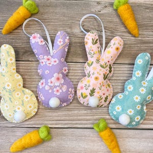 Pu&ograve; includere: Quattro ornamenti di coniglio in feltro con diversi motivi floreali. I conigli sono di colore lilla chiaro, rosa, giallo e verde acqua. Ogni coniglio ha una coda di pon pon bianca.