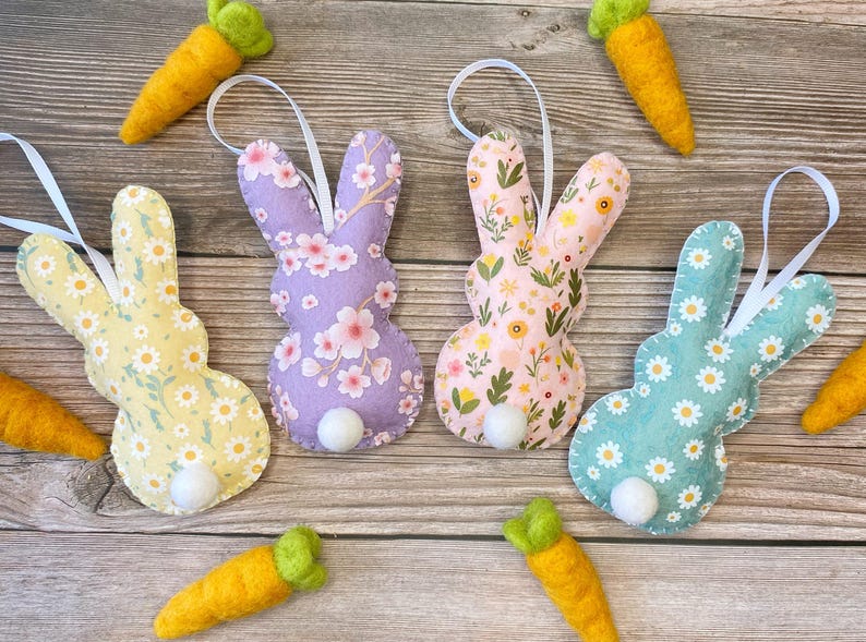 Pu&ograve; includere: Quattro ornamenti di coniglio in feltro con diversi motivi floreali. I conigli sono di colore lilla chiaro, rosa, giallo e verde acqua. Ogni coniglio ha una coda di pon pon bianca.