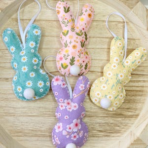 Pu&ograve; includere: Quattro ornamenti di coniglio in feltro con motivi floreali. I conigli sono rosa, viola, giallo e verde con pompon bianchi per le code.