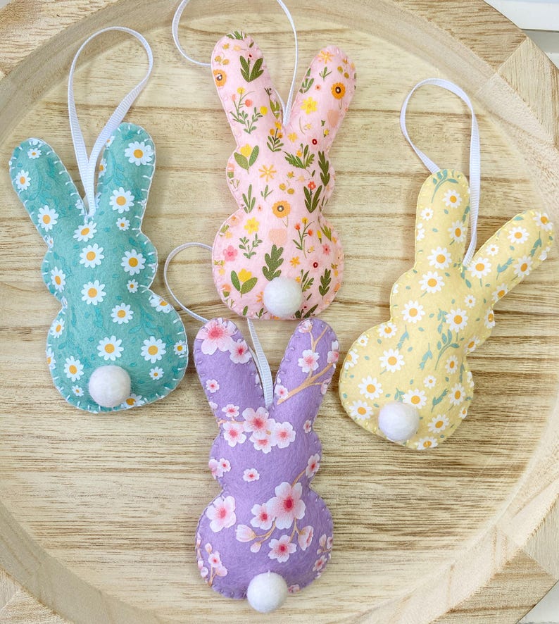 Pu&ograve; includere: Quattro ornamenti di coniglio in feltro con motivi floreali. I conigli sono rosa, viola, giallo e verde con pompon bianchi per le code.