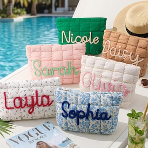 May include: Several quilted cosmetic bags in shades of green, pink, white, and blue floral, each embroidered with a name. A straw hat, sunglasses, and a magazine are also visible. The scene is set by a swimming pool.