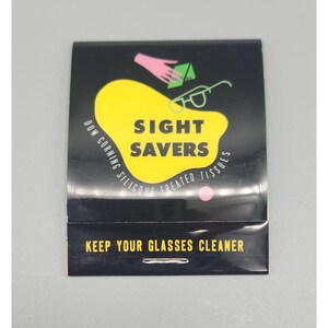 May include: A black packet of Sight Savers silicone-treated tissues. The packet features a yellow blob with the words "SIGHT SAVERS" in bold, black letters. The packet also has the text "KEEP YOUR GLASSES CLEANER".