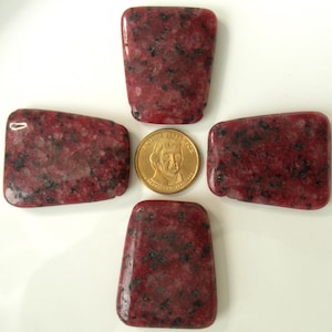 May include: Four red and black speckled stone shapes, each about the size of a US dollar coin. The stones are arranged in a cross pattern with a US dollar coin in the center.