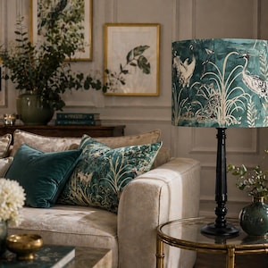Peut inclure: Un salon décoré avec un abat-jour teal orné de grues, une lampe assortie et des coussins décoratifs. Le canapé est beige, et la pièce comprend des impressions botaniques encadrées. Une petite table d'appoint avec un vase et un bol.