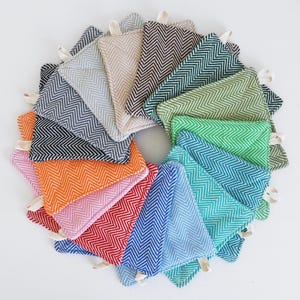 May include: A set of 12 colorful kitchen pot holders with a herringbone pattern. The pot holders are made of a soft, woven fabric and have a loop for hanging.