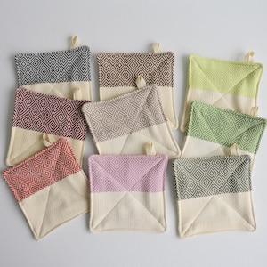 May include: Set of nine colorful kitchen pot holders with a geometric pattern. Each pot holder is made of a cream-colored fabric with a patterned square in the center.