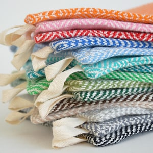 May include: A stack of colorful, woven fabric items with cream-colored ribbon loops. The fabrics display a chevron pattern in various colors, including orange, pink, red, blue, green, and gray. The items appear to be small, possibly for crafting or home decor.