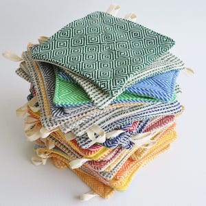 May include: A stack of colorful woven pot holders with a green and white geometric pattern on top. The pot holders have a simple design and are made of a soft, natural material.