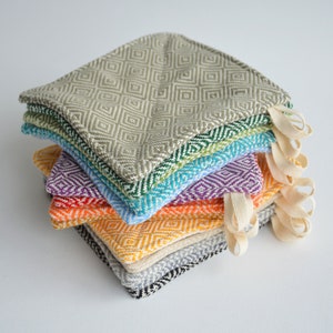 May include: A stack of eight colorful woven pot holders with a diamond pattern. The pot holders are made of cotton and have a loop for hanging.