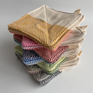 May include: A stack of colorful, square pot holders. Each pot holder features a diamond pattern and a two-tone design, with one half in a solid color and the other in cream. Colors include yellow, pink, red, green, blue, and gray.