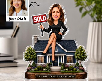 May include: A custom acrylic desk ornament featuring a cartoon-style woman in a black suit sitting on a blue house roof. She holds a red sign that says SOLD. The base is wood-toned with the text SARAH JONES - REALTOR printed on a gold plaque.