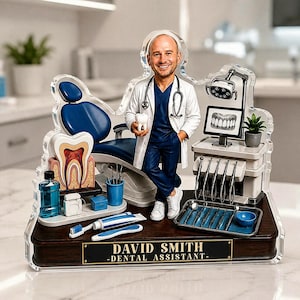 May include: A custom acrylic display featuring a dental assistant figure in a white coat and blue scrubs, standing next to a blue dental chair, equipment, and tools. A plaque at the base reads DAVID SMITH - DENTAL ASSISTANT - with a tooth model.