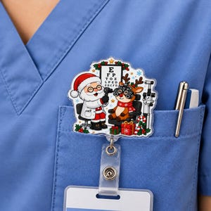 May include: A badge reel featuring a cartoon illustration of Santa Claus performing an eye exam on a reindeer. Santa wears a white coat and glasses, while the reindeer wears a red scarf and sits in an exam chair. An eye chart is visible.