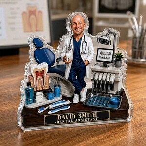 May include: A custom acrylic desk ornament featuring a miniature dentist figure in a white coat and blue scrubs, holding a tooth model. The display includes a dental chair, a monitor with an X-ray, tools, and a plaque reading DAVID SMITH - DENTAL ASSISTANT.