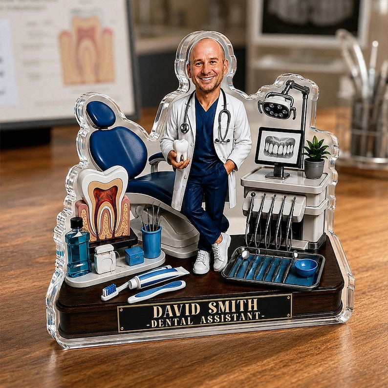 May include: A custom acrylic desk ornament featuring a miniature dentist figure in a white coat and blue scrubs, holding a tooth model. The display includes a dental chair, a monitor with an X-ray, tools, and a plaque reading DAVID SMITH - DENTAL ASSISTANT.